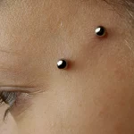 A surface piercing involves inserting a barbell or a piece of jewelry just under the surface of the skin, creating two visible holes at the entry and exit points. This differs from traditional piercings, which penetrate through a body part (like an ear or nostril). Surface piercings are often performed on flat or curved surfaces, such as the back of the neck (nape), chest, hips, or even the face.