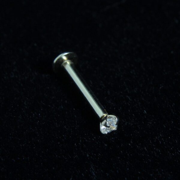 Close-up view of a 14kt gold 16g threadless labret with a clear gem on a black velvet background.
