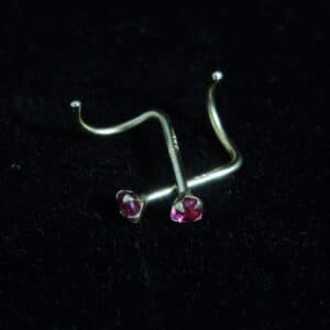 Two 14kt yellow gold nose screws with red gemstones set in claw settings, displayed against a black velvet background.