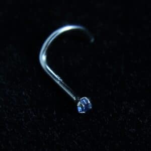 A 14kt white gold nose curve featuring a genuine sapphire gemstone in a claw setting, placed on a black velvet background.